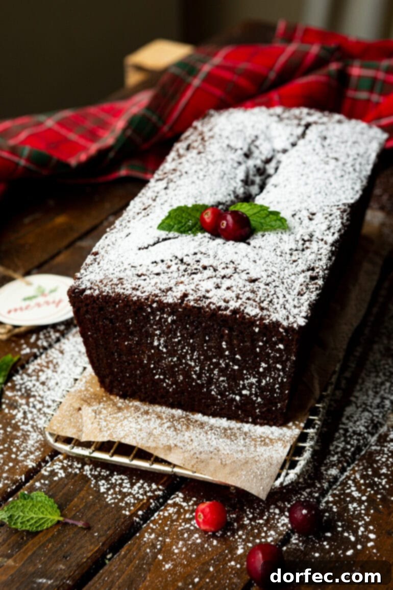Classic Gingerbread Loaf 12 A charming photo of a whole gingerbread loaf, artfully dusted with powdered sugar and elegantly garnished with whole cranberries and fresh mint leaves, ready to be served.