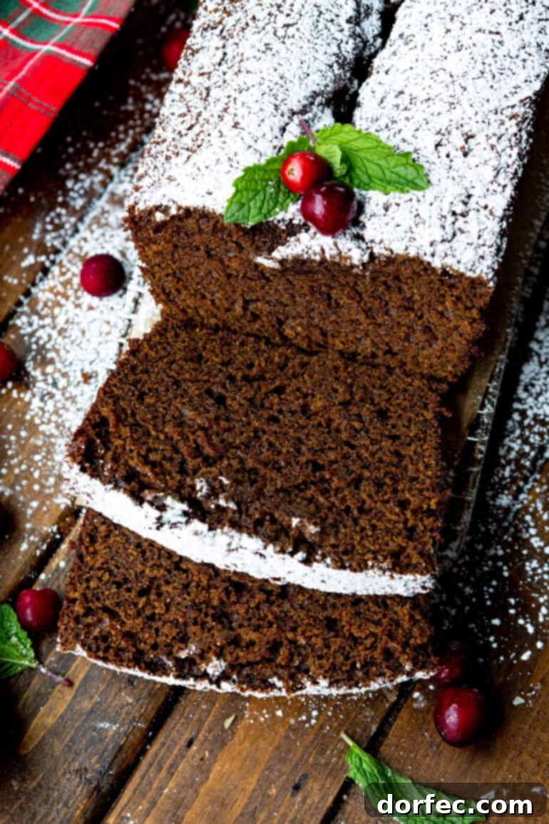 Classic Gingerbread Loaf 14 A inviting photo of a gingerbread loaf with several slices already cut, artfully topped with powdered sugar and garnished with two whole cranberries and fresh greenery.