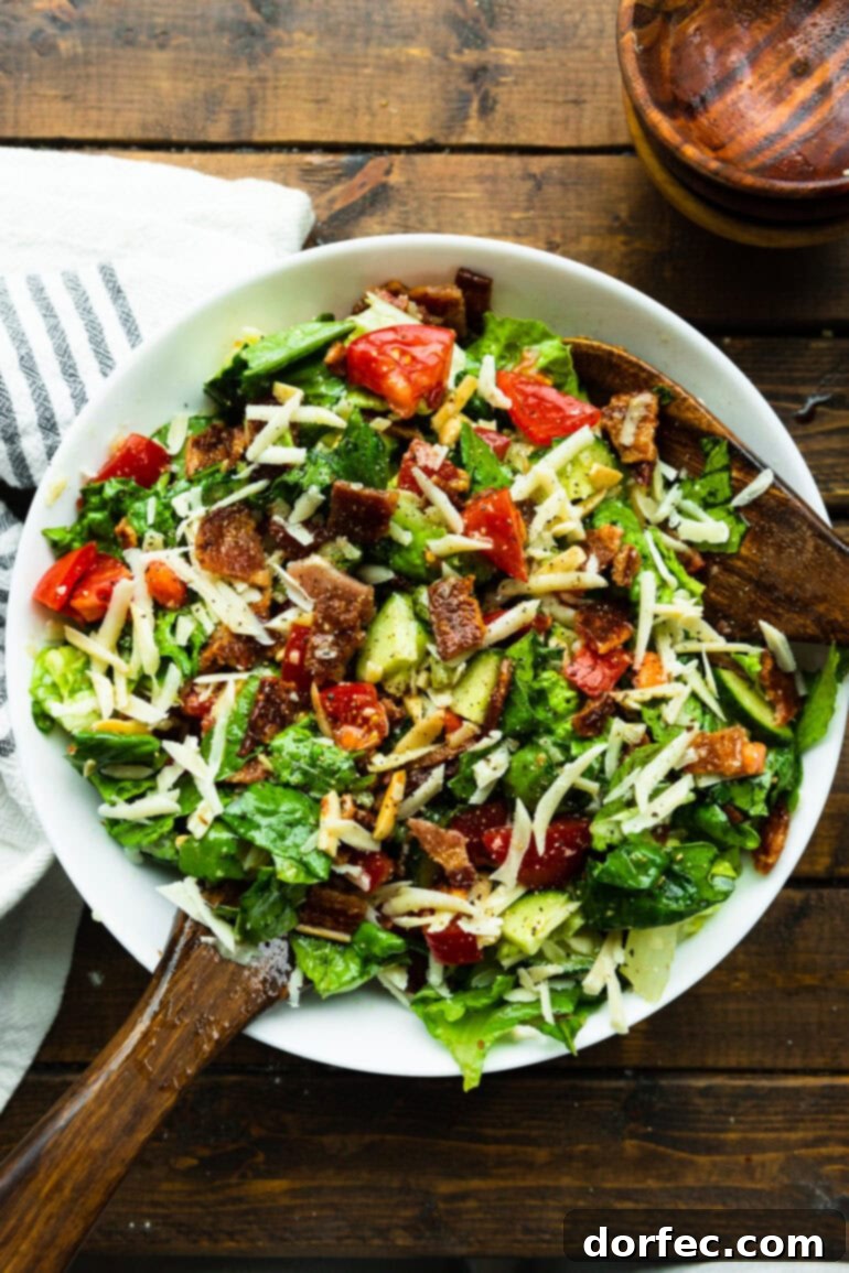 A large serving bowl showcasing a vibrant mix of chopped romaine lettuce, sweet tomatoes, crunchy slivered almonds, fresh cucumber, and savory Manchego cheese before tossing.