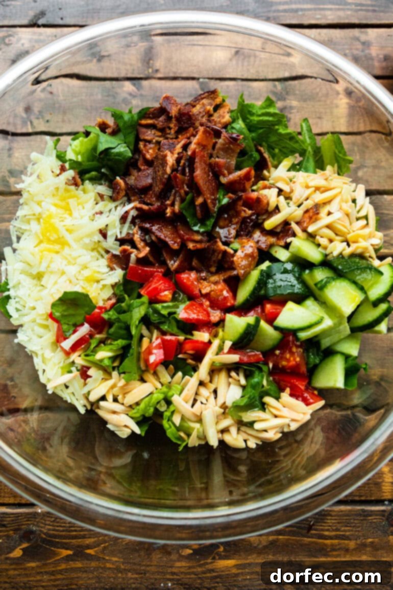 A large glass bowl filled with all the colorful ingredients for Salad de Maison, layered beautifully and ready for its final toss with the dressing.
