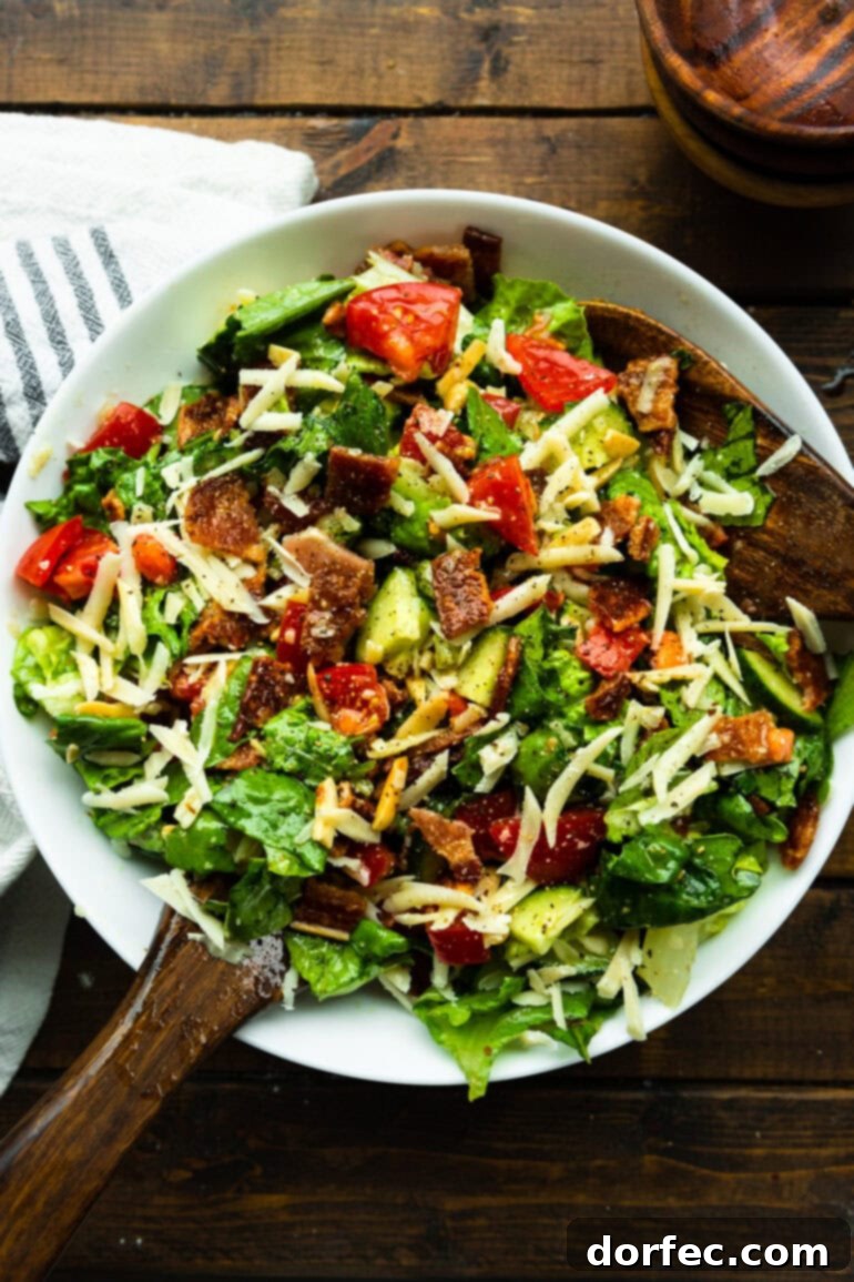 A vibrant green salad, expertly tossed and garnished with bright red tomatoes, savory bacon crumbles, and crisp cucumber slices, glistening with a lemon vinaigrette.