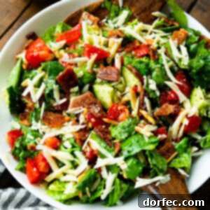 a photo of a large bowl full of a green salad with slivered almonds, tomatoes, and bacon crumbles