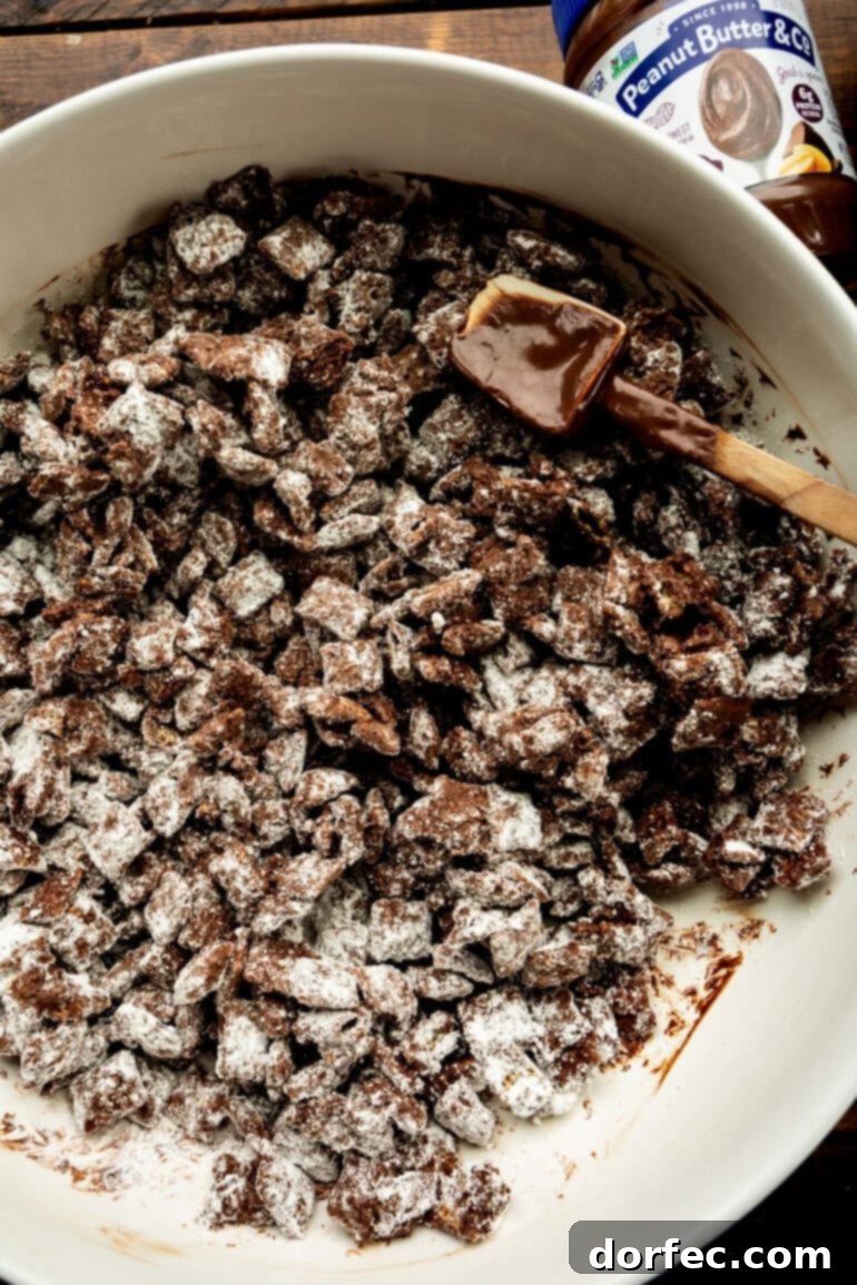 dark chocolate coated chex cereal being stirred in a white mixing bowl with a rubber spatula