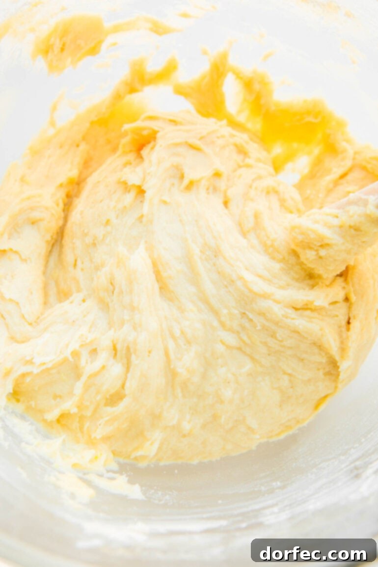 Zesty Lemon Glazed Loaf 5 Close-up shot of a creamy, pale yellow lemon pound cake batter swirling in a mixing bowl, showcasing its smooth texture before baking.