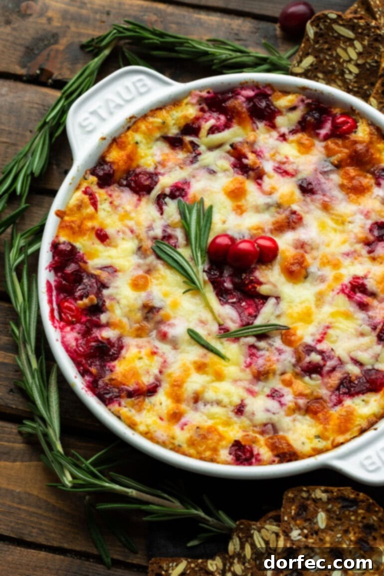 cheesy cranberry cream cheese dip in a circular cast iron baking dish topped with fresh rosemary and whole cranberries