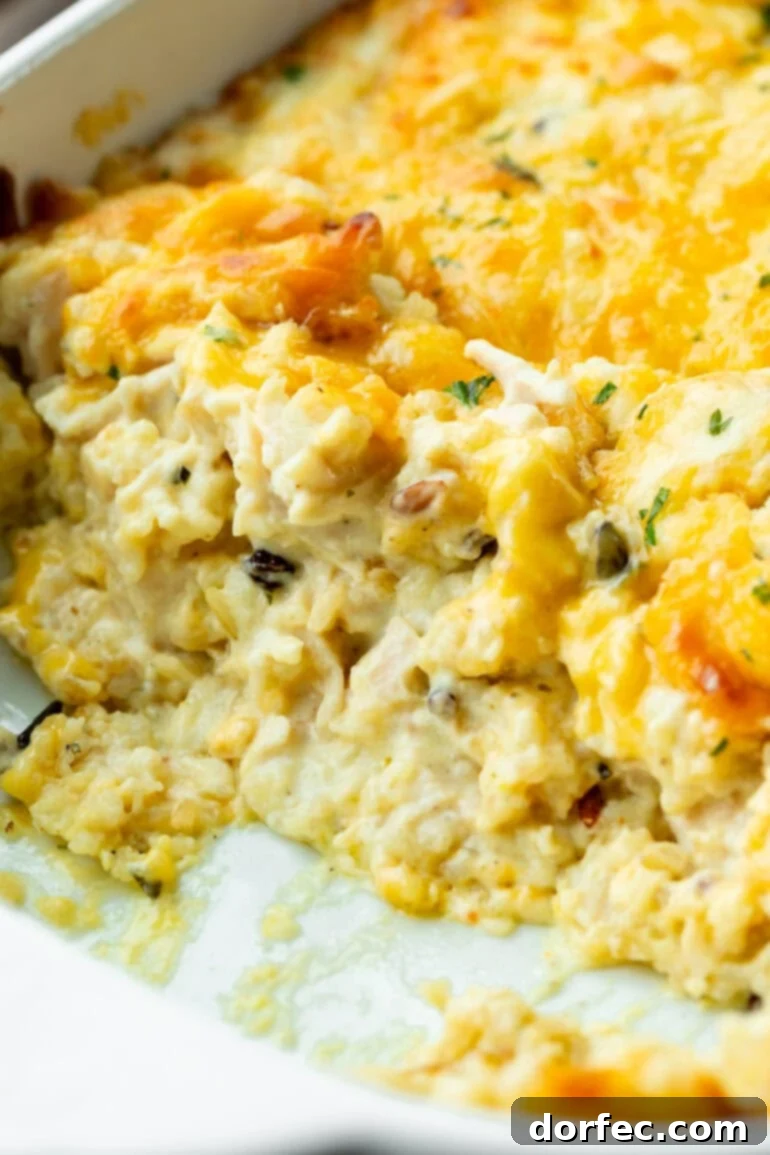Super Creamy Cheesy Chicken and Rice Casserole 2 A glistening photo of creamy chicken and rice casserole, generously topped with golden melted cheese and a sprinkle of fresh green herbs, ready to be served.