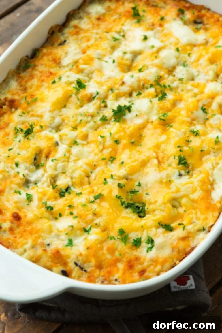 Super Creamy Cheesy Chicken and Rice Casserole 8 A full white casserole dish of baked chicken and rice casserole, topped with golden-brown melted cheese and a generous sprinkle of fresh chopped parsley, ready for serving.