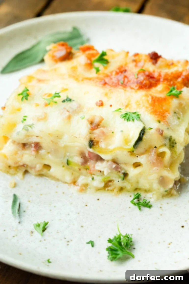 A photo of a serving of pancetta vegetable lasagna with white sauce sitting on a white dinner plate, garnished with fresh herbs.