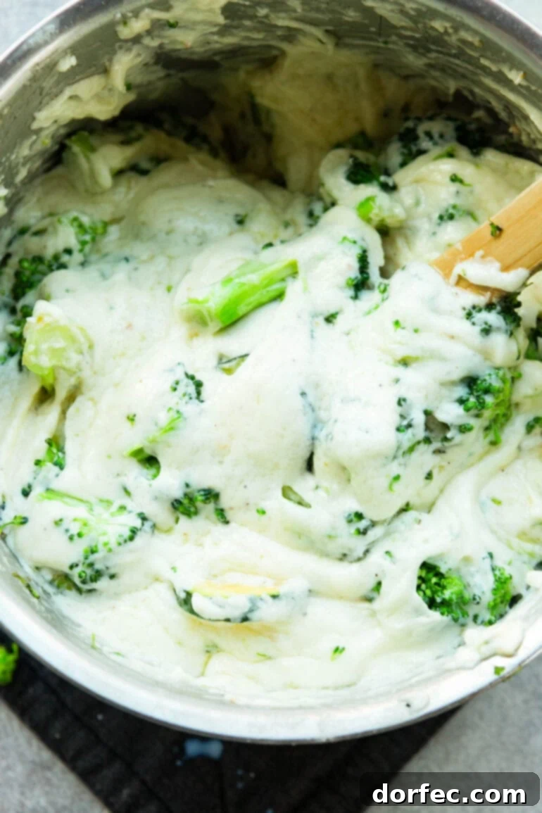 A photo of cooked broccoli and zucchini being stirred into a creamy white béchamel sauce in a pan, ready for layering.