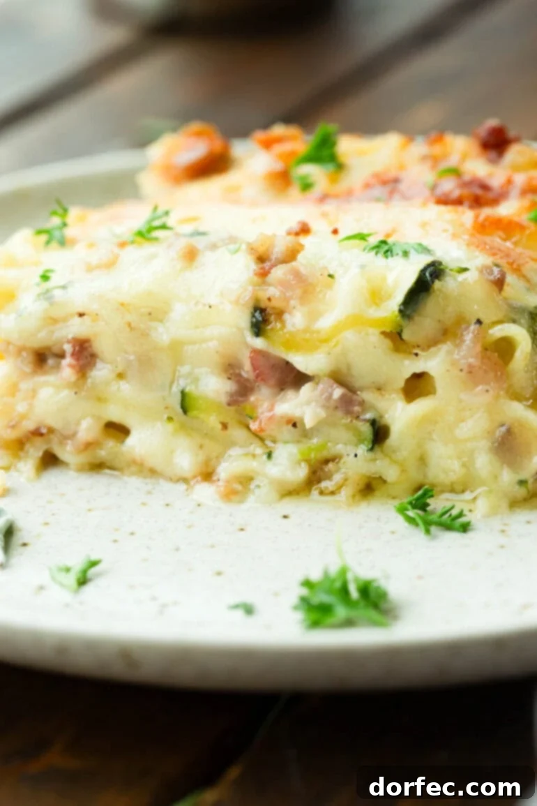 A photo of a slice of pancetta vegetable lasagna with white sauce sitting on a dinner plate, ready to be enjoyed.