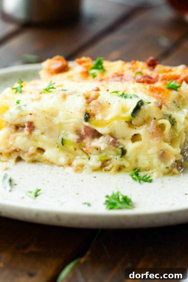 A photo taken from the side of a piece of pancetta vegetable lasagna sitting on a dinner plate, showcasing all the cheesy, creamy layers.