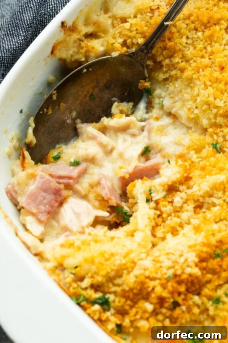A serving spoon lifting a generous portion of creamy Chicken Cordon Bleu Casserole, showcasing the golden breadcrumb topping and rich, cheesy filling.