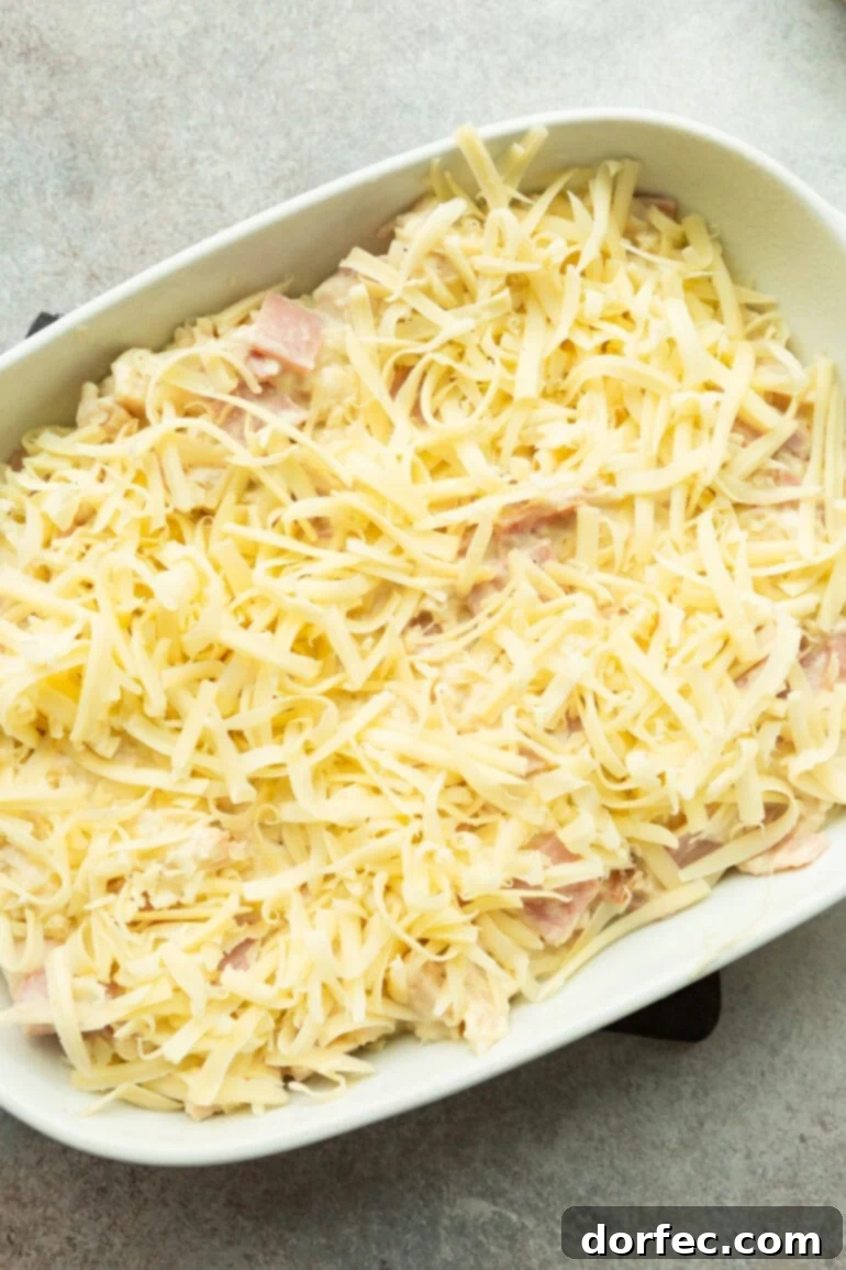 An unbaked Chicken Cordon Bleu Casserole, topped with a generous layer of shredded Swiss cheese, ready to go into the oven.