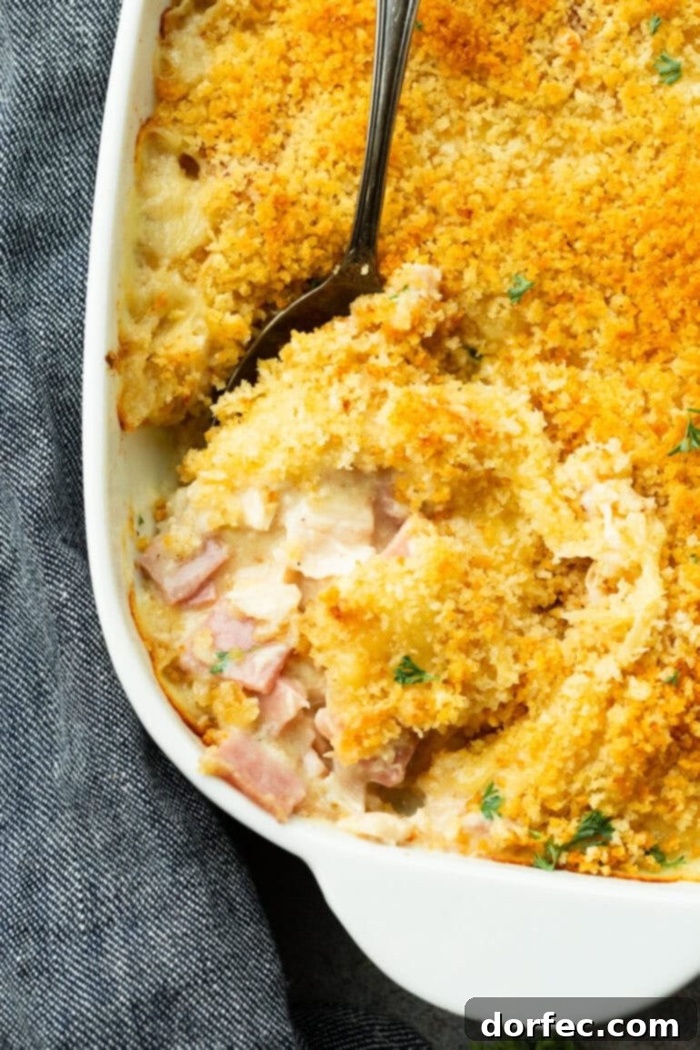 A large serving spoon scooping out a portion of creamy Chicken Cordon Bleu Casserole from a baking dish, highlighting the rich texture.