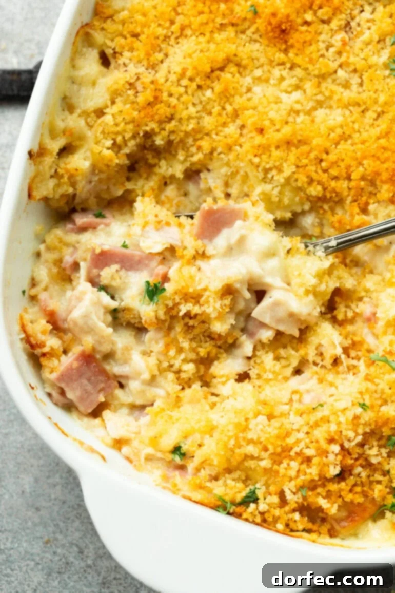 A person scooping a generous serving of creamy Chicken Cordon Bleu Casserole from a large baking dish, ready to be enjoyed.
