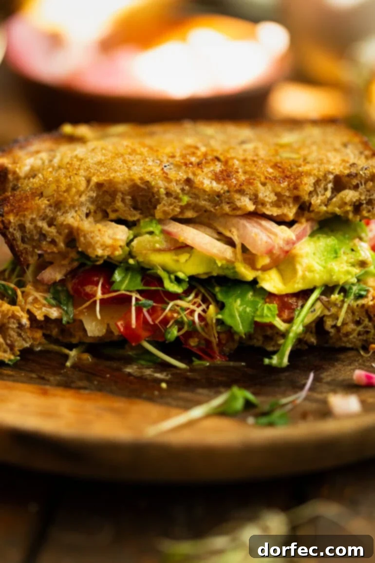 A photo of a gourmet avocado sandwich with toasted multigrain bread, bean sprouts, pickled red onions, sliced avocado, and fresh arugula, beautifully presented for a healthy lunch.