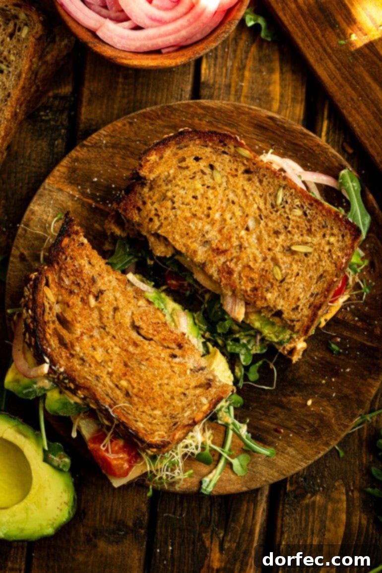 An overhead shot of a delicious avocado sandwich, sliced in half and served on a rustic wooden plate, showcasing its vibrant layers and inviting texture. Perfect for a healthy, quick lunch.
