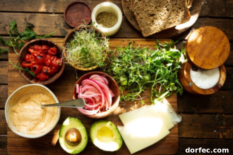A vibrant flat lay photo showcasing all the fresh ingredients needed for a delicious avocado sandwich, including sliced avocado, Manchego cheese, microgreens, charred cherry tomatoes, arugula, and a bowl of spicy mayo.