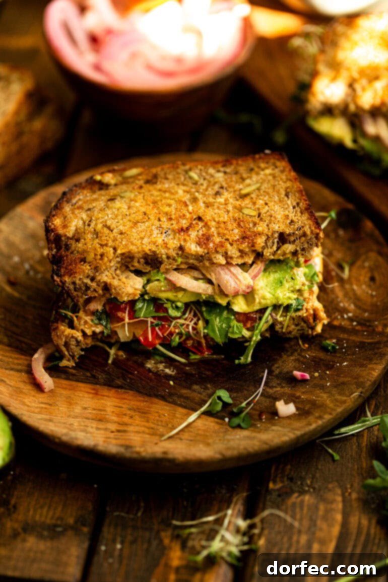 A close-up shot of one half of an avocado sandwich resting on a wooden plate, highlighting the crispy toasted bread and the fresh, vibrant layers inside, ready to be enjoyed.