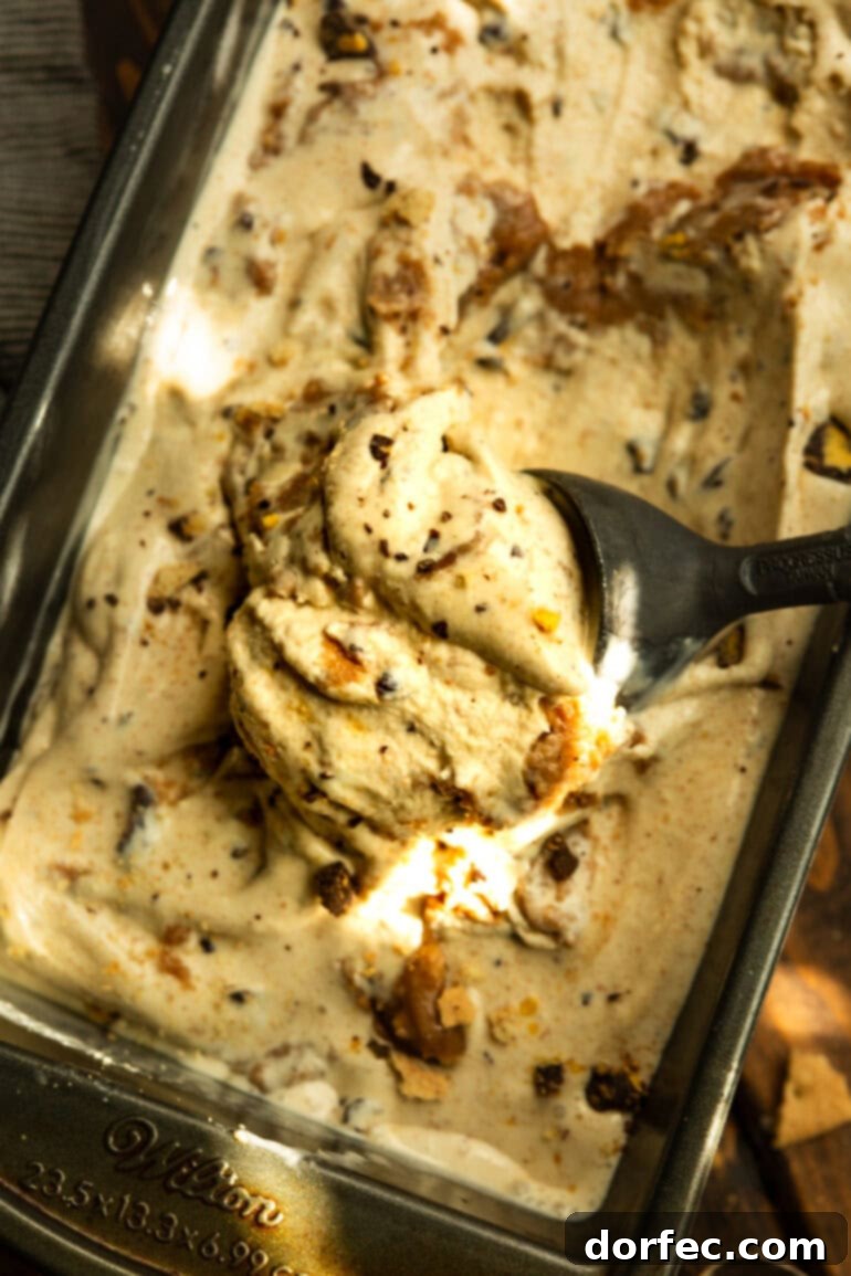 A hand scooping a generous serving of Graham Canyon ice cream from a bread loaf pan, showing the delightful layers of ice cream and swirl.