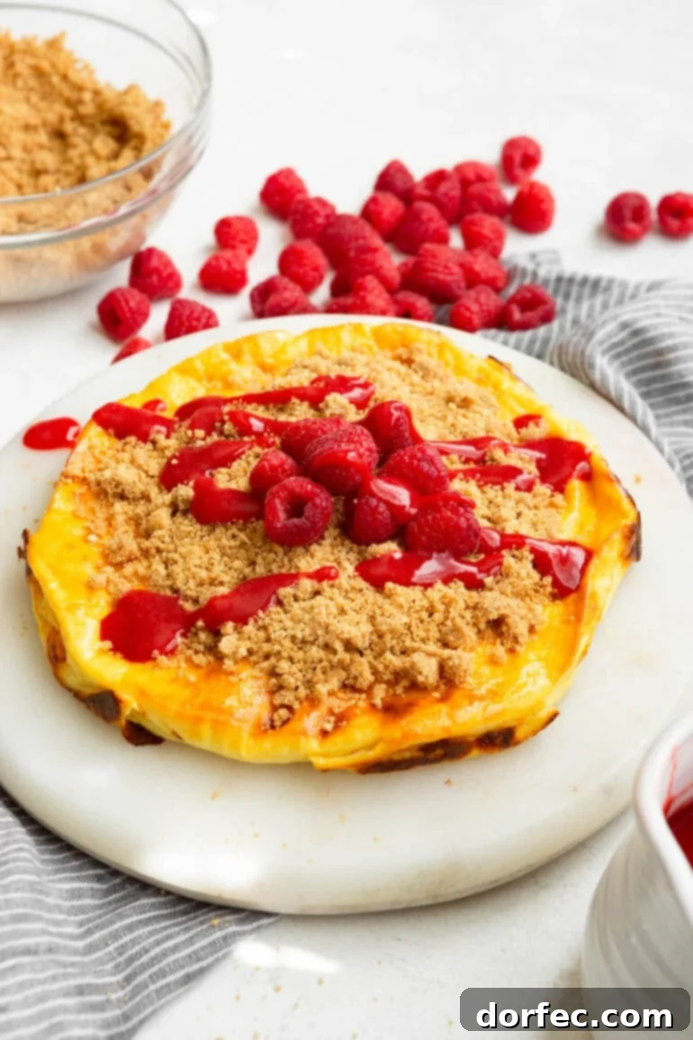 Creamy Baked Yogurt Cheesecake 5 A photo of a baked yogurt cake topped with graham cracker crumble, whole raspberries, and raspberry sauce.