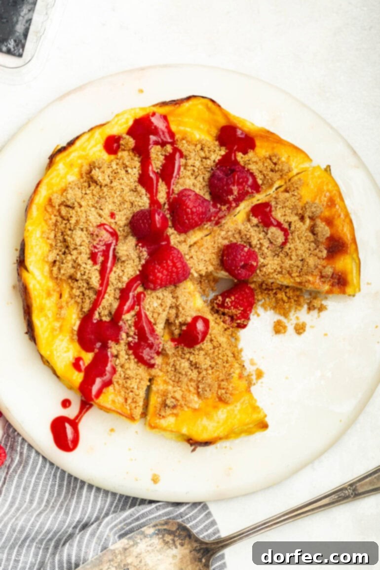 Creamy Baked Yogurt Cheesecake 7 A photo taken over the top of a baked yogurt with a slice removed, topped with raspberry sauce, graham cracker crumble, and fresh raspberries.