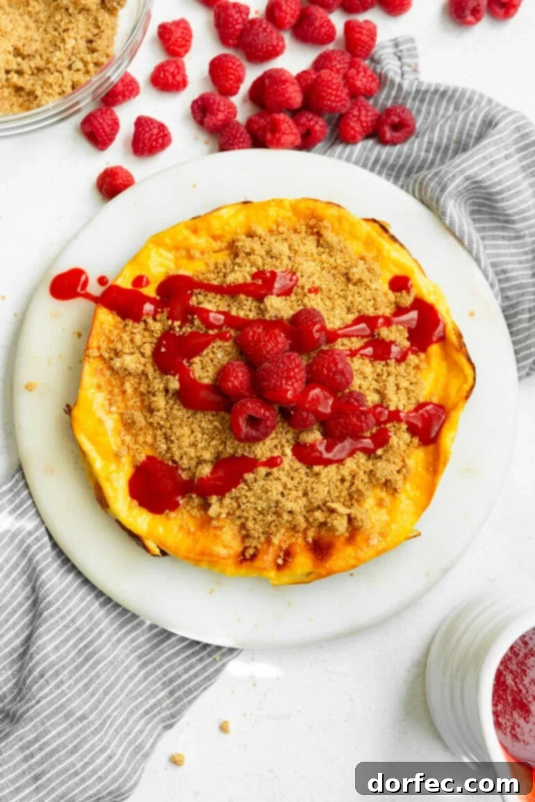 Creamy Baked Yogurt Cheesecake 8 A photo taken over the top of a circular baked yogurt topped with graham cracker crumble, raspberry sauce, and whole raspberries.