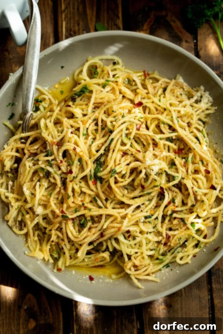 A large plate of cooked spaghetti aglio e olio, tossed with hot oil, fresh garlic, and green herbs.