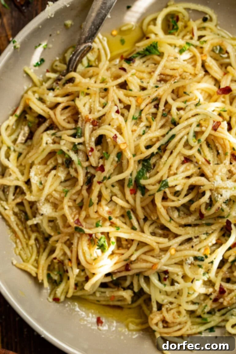 A close-up photo of a bowl of spaghetti aglio e olio, showing the glossy pasta strands intertwined with minced garlic and green herbs.
