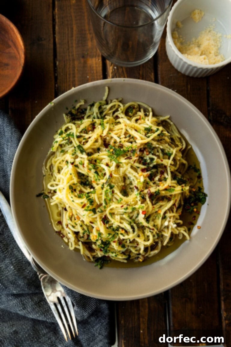A large serving bowl overflowing with spaghetti aglio e olio, generously topped with parmesan cheese, herbs, and red pepper flakes.