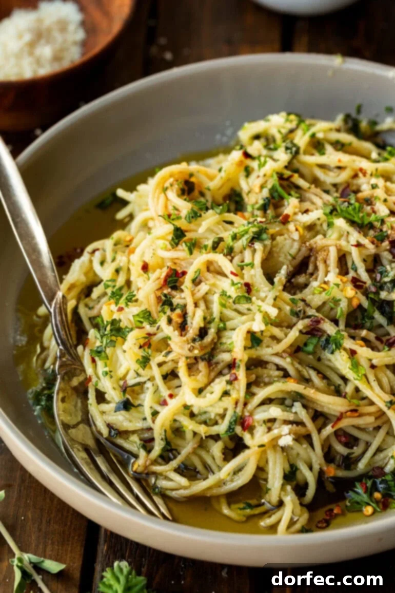 A beautifully plated bowl of spaghetti aglio e olio, crowned with a generous sprinkle of freshly grated Parmesan cheese and vibrant green herbs.