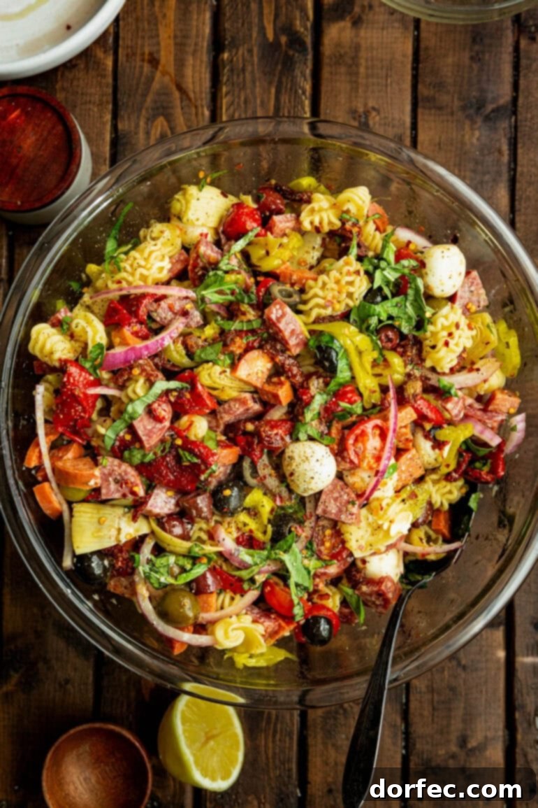 A large glass bowl overflowing with antipasto pasta salad, featuring a generous drizzle of homemade herb dressing on top, ready to be served.