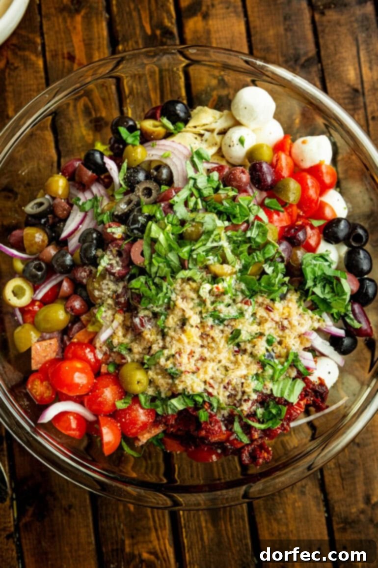 A large glass bowl filled with the vibrant, unmixed ingredients for antipasto pasta salad, awaiting the dressing and a final toss.