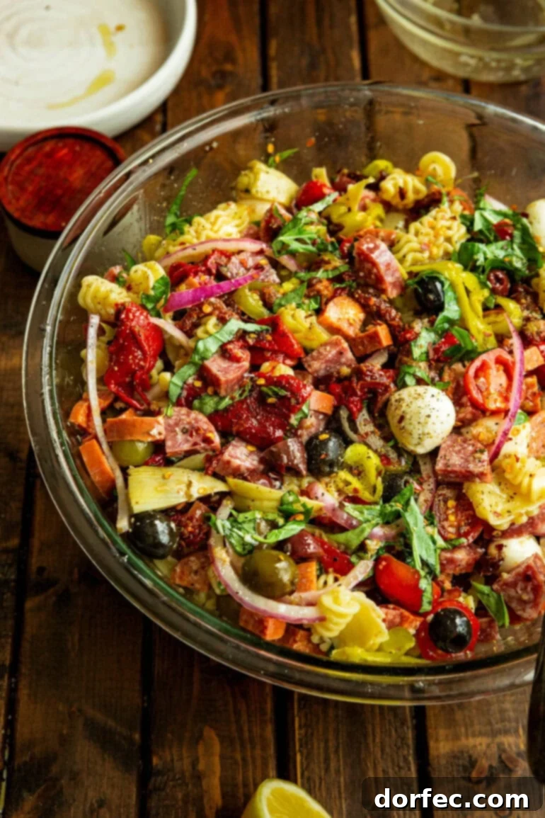 A large, beautifully presented antipasto pasta salad in a clear glass serving bowl, showcasing its colorful ingredients.
