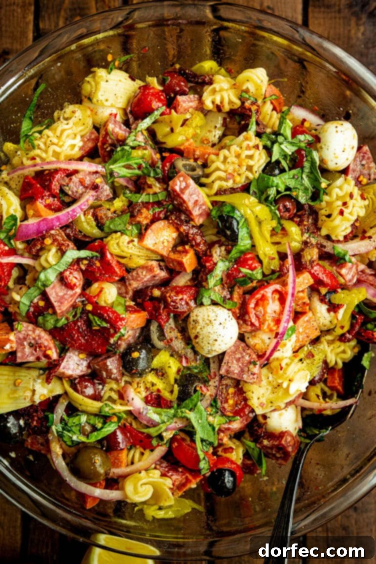 An inviting overhead shot of a large glass serving bowl filled with colorful antipasto pasta salad.