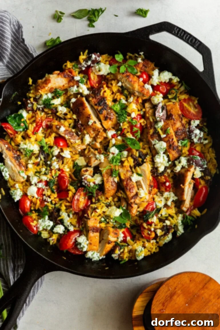 A cast iron pan with cooked Greek lemon rice, roasted grape tomatoes, fresh herbs, crumbled feta, and perfectly grilled chicken thighs, ready to be served for a healthy Mediterranean dinner.