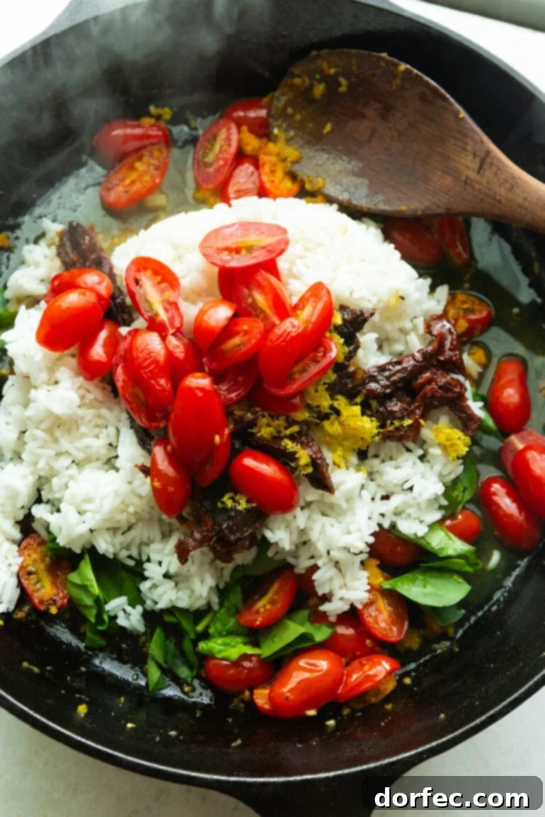 A cast iron skillet, sizzling hot, showcasing a vibrant mix of lemon rice, sweet grape tomatoes, tangy sun-dried tomatoes, aromatic herbs, and glistening olive oil, hinting at the delicious flavors within.