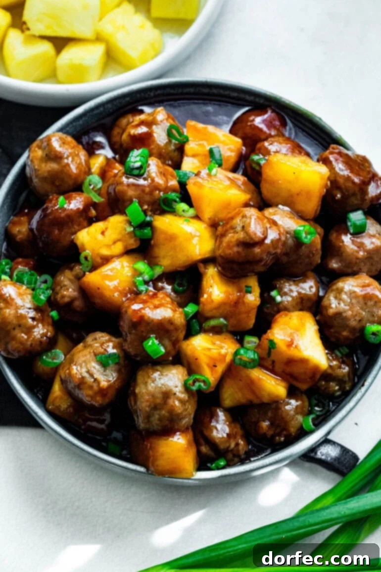 a plate of saucy hawaiian meatballs with chunks of pineapple and chopped green onions