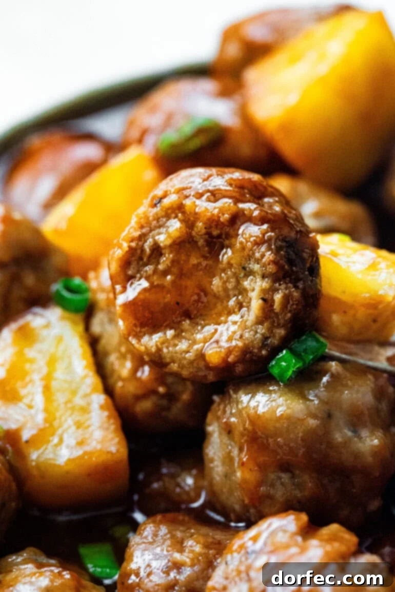 close up of the cross-section of a hawaiian meatball with other meatballs and pineapple chunks around it
