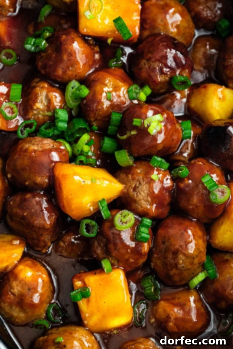 a large pot of saucy hawaiian meatballs with pineapple chunks and chopped green onions