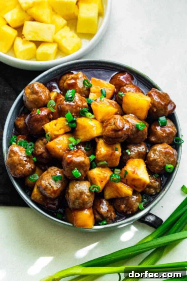 a large serving bowl of saucy hawaiian meatballs mixed with pineapple chunks and topped with chopped green onions