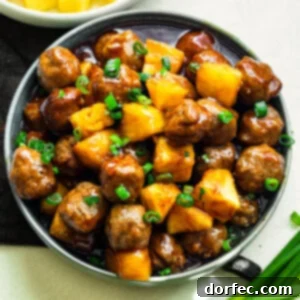 a large serving bowl of saucy hawaiian meatballs mixed with pineapple chunks and topped with chopped green onions