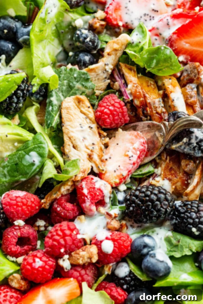 A close-up view of a tossed Berry Avocado Chicken Salad, highlighting the strips of chicken breast, crunchy candied pecans, and a generous drizzle of creamy poppyseed dressing, ready to be enjoyed.
