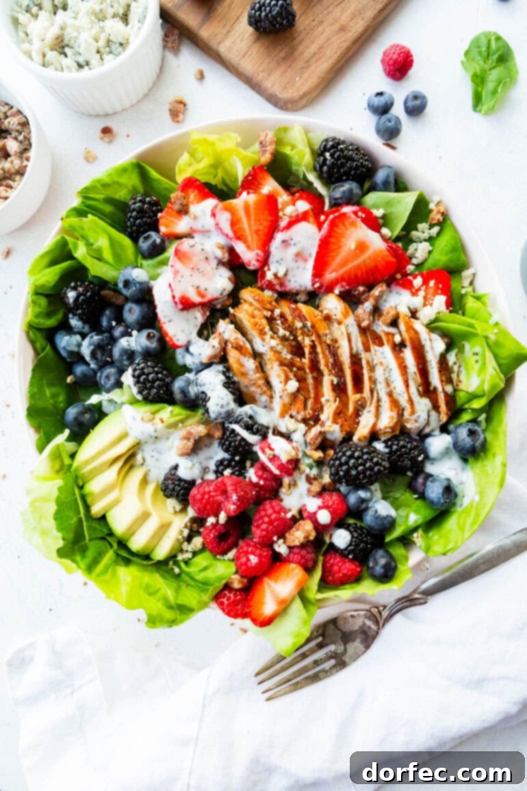 A vibrant bed of crisp butter lettuce topped with an assortment of fresh strawberries, raspberries, blackberries, and blueberries, alongside perfectly sliced chicken breast, creamy avocado, and a generous drizzle of poppyseed dressing.