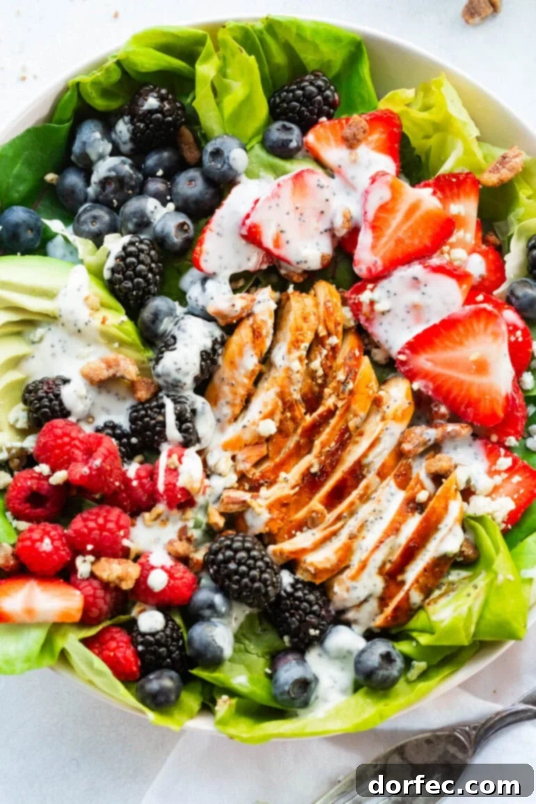 A beautifully composed bowl of Berry Avocado Chicken Salad, topped with succulent chicken, crunchy candied pecans, and a generous drizzle of creamy poppyseed dressing, ready to be enjoyed.