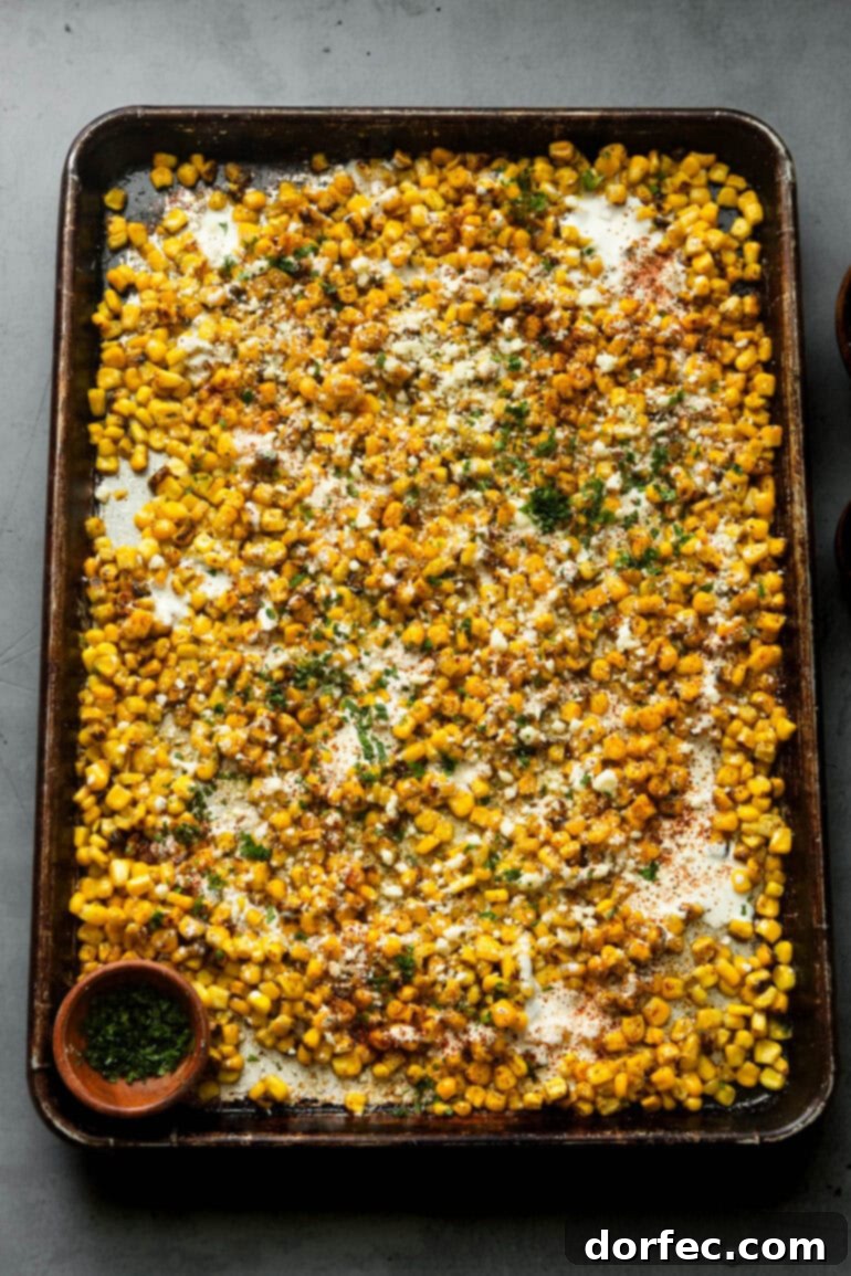 Sheet Pan Oven Elote 4 a photo of a baking sheet loaded with roasted corn sprinkled with cotija cheese, chili powder and chopped cilantro