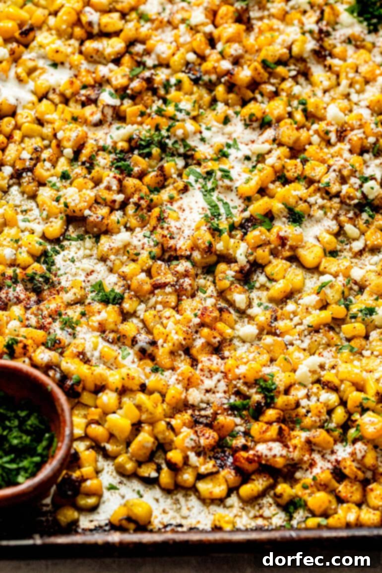 Sheet Pan Oven Elote 5 a photo of roasted corn mixed with mexican crema, chili powder, cotija cheese and chopped cilantro spread out on a sheet pan