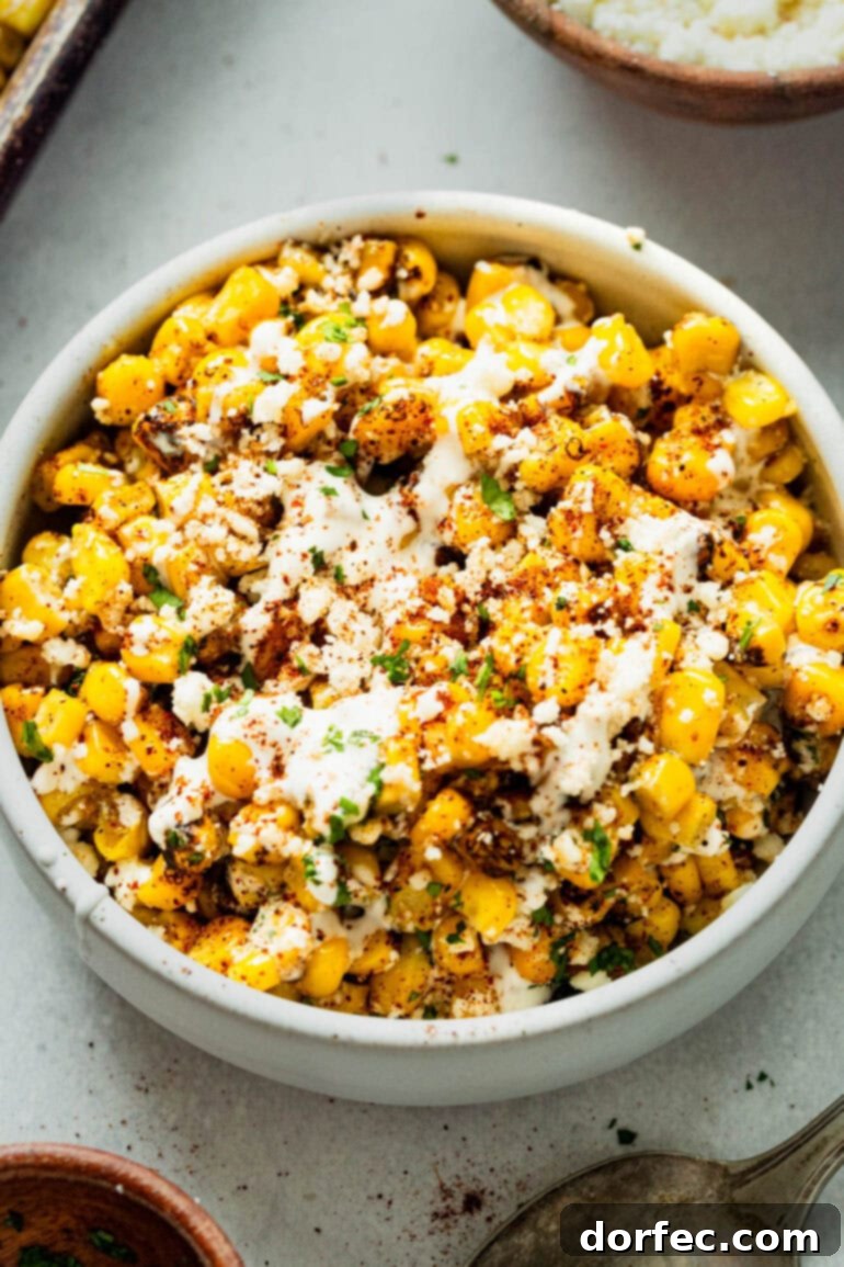 Sheet Pan Oven Elote 6 a photo of a white serving bowl full of roasted mexican street corn topped with crumbled cotija cheese, chili powder and fresh cilantro