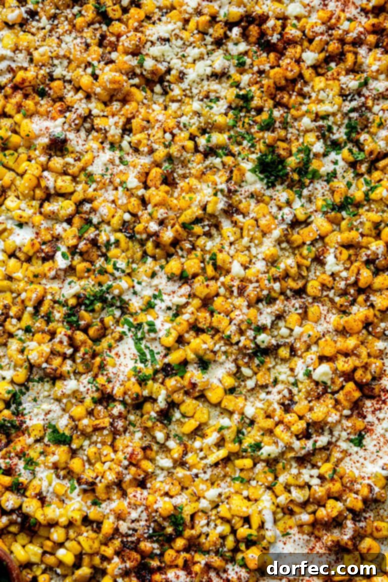 Sheet Pan Oven Elote 7 a photo of a sheet pan full of roasted corn topped with mexican crema, cotija cheese, chili powder and fresh cilantro