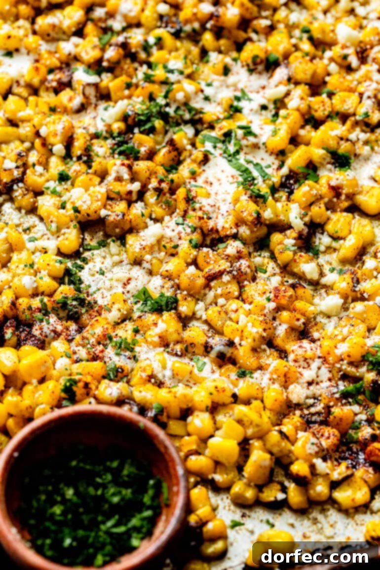 Sheet Pan Oven Elote 8 a photo of a sheet pan filled with roasted corn mixed with cotija cheese, mexican crema, chili powder and cilantro